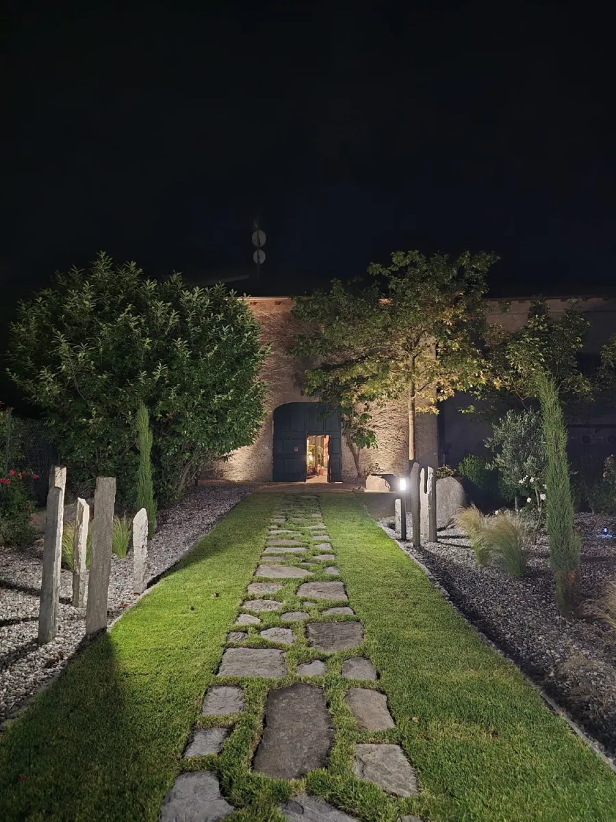 Visione notturna con illuminazione di un viale d'ingresso con pavimentazione in prato, passi persi in lose e menir in pietra
